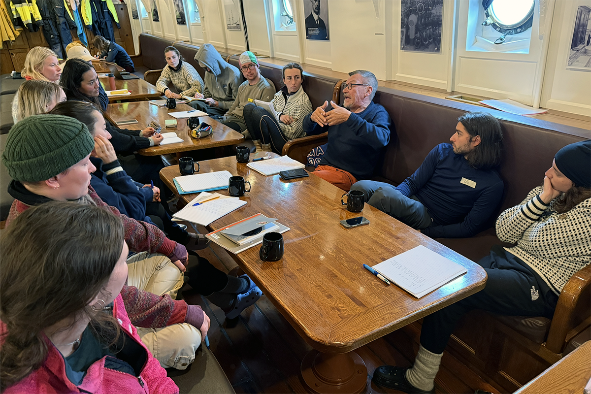 Mange personer rundt flere bord i en messe på et skip.